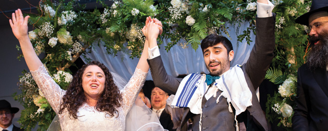 Bride and groom hold hands and raise their arms in the air joyfully